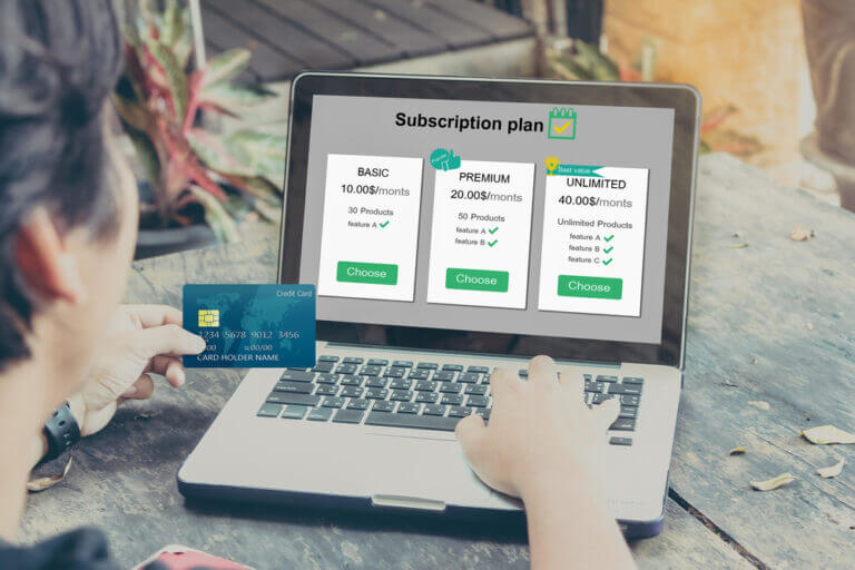 Nell'immagine si vede una persona al laptop nell'atto di scegliere un abbonamento ad una vpn, con carta di credito in mano, pronto per pagare.